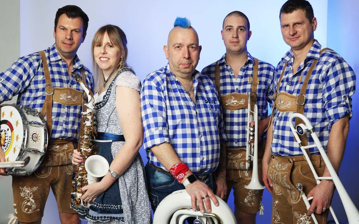 Five band members posed in blue check shirts, lederhosen and a dirndl, holding a drum, saxophone, white tuba, trumpet and trombone