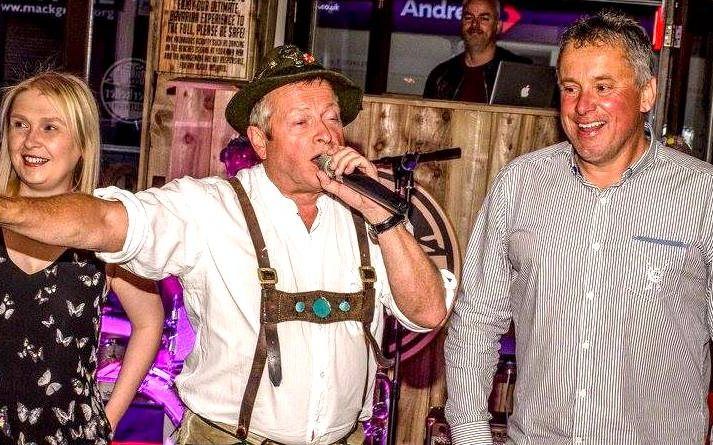 The singer of Karl's Bavarian Brass in lederhosen and a feathered hat, pointing into the crowd